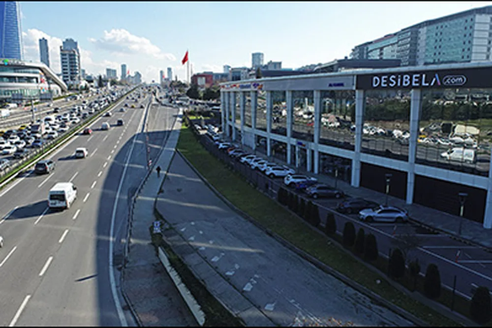 Desibela tabelalı mağaza binası, önünde otoyol ve park alanı