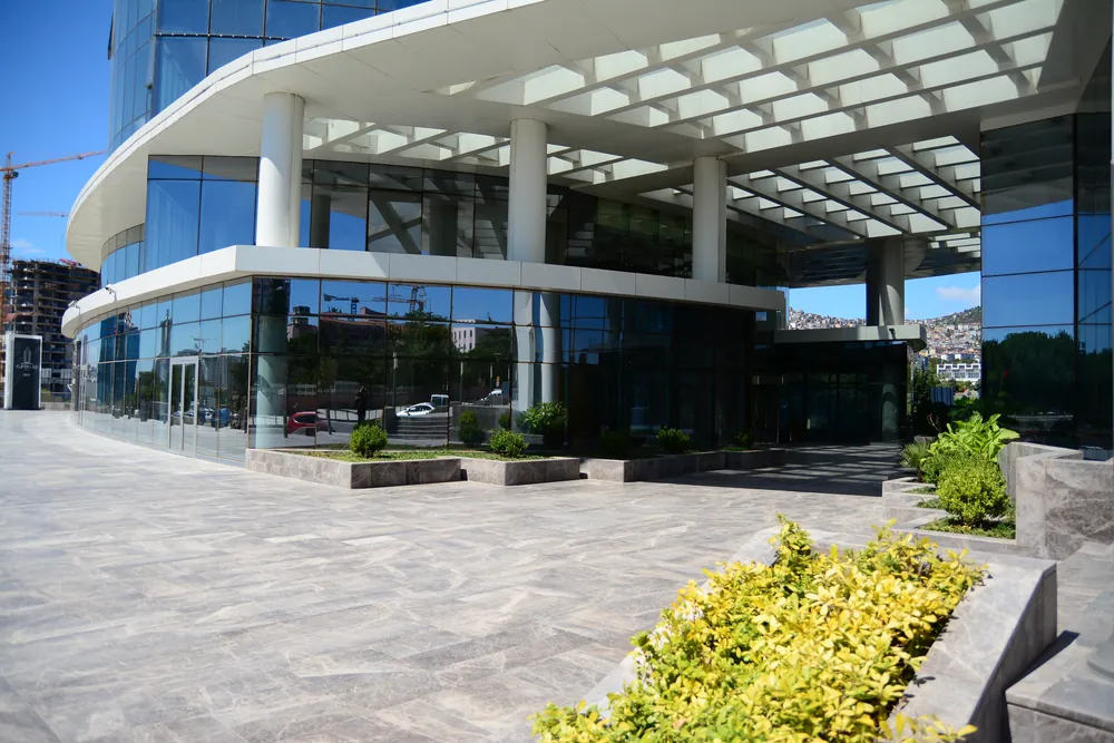 Kuriş Kule giriş saçağı altında cam cepheli alçak blok ve peyzaj
